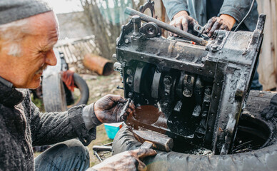 Fototapeta na wymiar elderly man tuning a car engine at home in a garage, customizing an engine in a village.