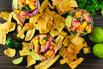 Dishes of Salmon Ceviche with Mango Surrounded with Plantain Chips: Bowls of salmon ceviche with plantain chips and ingredients on a wooden table © Candice Bell
