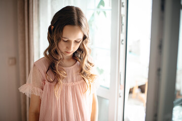 A little girl in a pink dress stands and combs her brown curled hair