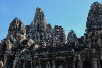 General view of the ancient Bayon Temple with stone towers and human faces in Cambodia on a sunny day.