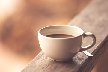 A white cup of coffee on wooden with morning light background texture