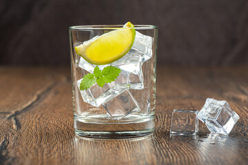 Ice cubes, lime slice and mint leaves in a glass on a wooden background.