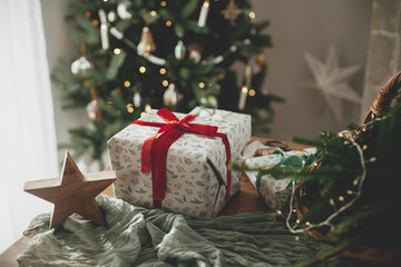 Stylish wrapped christmas gifts, rustic basket with fir branches and modern decorations against...