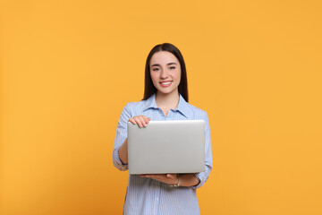 Fototapeta premium Smiling young woman with laptop on yellow background