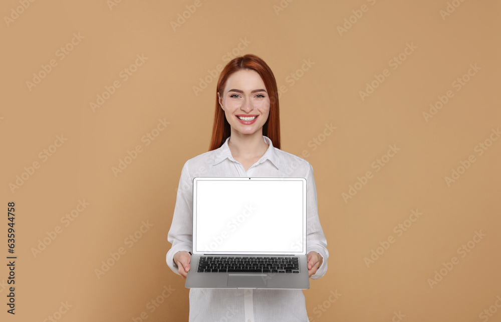 Wall mural Smiling young woman showing laptop on beige background