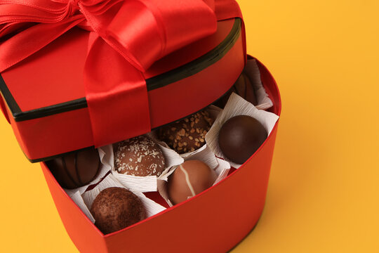 Heart shaped box with delicious chocolate candies on yellow background, closeup
