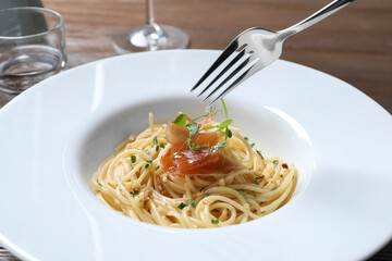 Eating tasty spaghetti with prosciutto and microgreens at table, closeup. Exquisite presentation of pasta dish