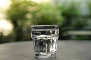 Glass of fresh water on grey table outdoors, closeup