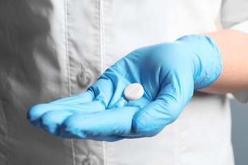 Doctor in medical glove holding pill, closeup view