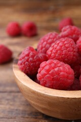 Tasty ripe raspberries in bowl on wooden table, closeup