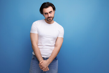 shy young brunette guy in white t-shirt on studio background
