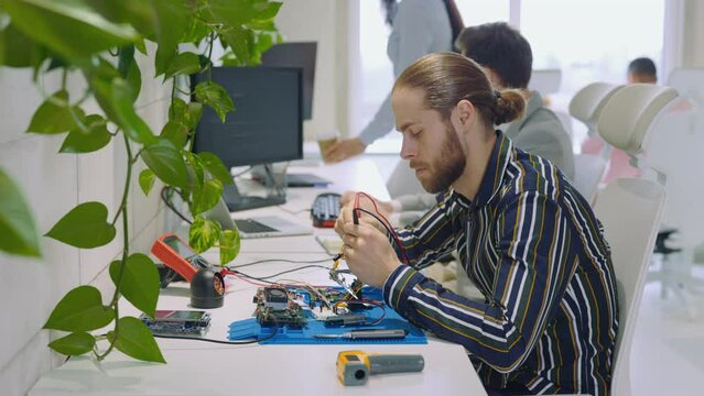 Electronics Maintenance Engineer in Office Working in Tablet, Soldering Iron Mother Board.