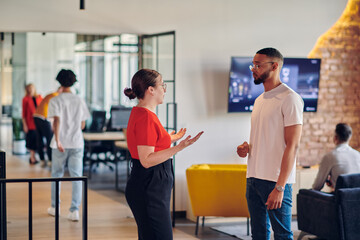 Obraz premium Young business colleagues, including an African American businessman, engage in a conversation about business issues in the hallway of a modern startup coworking center, exemplifying dynamic problem