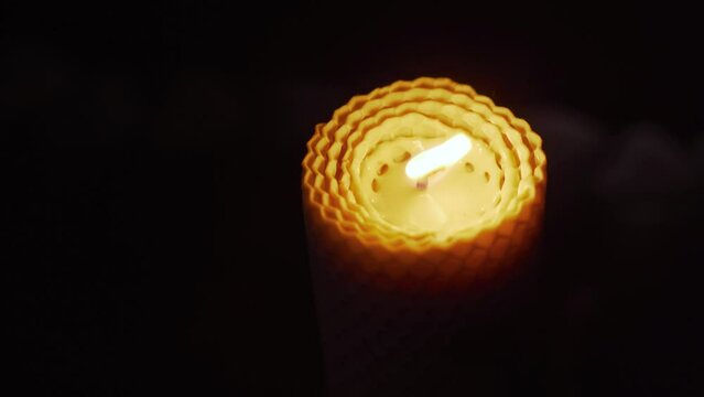 A candle made of natural beeswax burns in the dark.