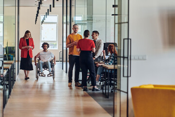 A group of young business people in a modern glass-walled office captures the essence of diversity and collaboration, while two colleagues, including an African American businessman in a wheelchair