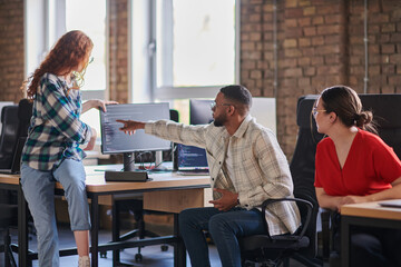 A diverse group of young business individuals congregates in a modern startup coworking center,...