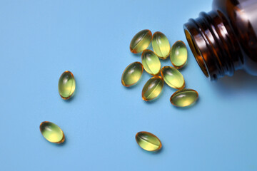 Yellow capsules scattered from a jar on a blue background