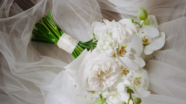 A wedding bouquet of white flowers lies on a snow-white veil. Morning preparations of the newlyweds. Flower arrangement in the bedroom.