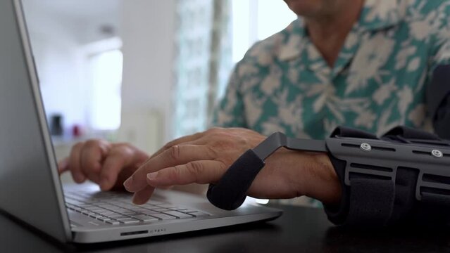 Man with adjustable articulated elbow orthosis typing on laptop keyboard