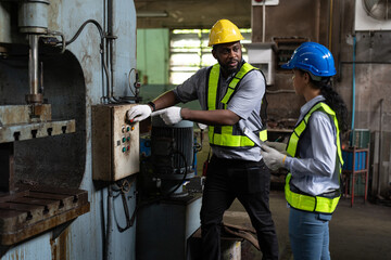 African American male and female engineers in safety vest and helmet working at heavy metal industrial factory. Two technician foreman discussing for checking and repairing machine at factory.