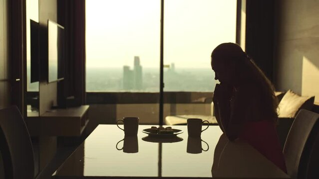 Silhouette sad unhappy woman alone at home.Lonely Person sitting, think about his loss of loved.Table, two mugs, coffee.Woman want to see your beloved husband.Concept loss love one loneliness, misses