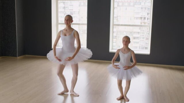 Wide shot of dancers in white tutu skirts and leotards jumping in ballet style during lesson at studio