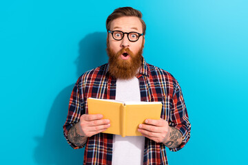 Photo of amazed funny young student guy beard glasses holding orange copybook shocked reaction...