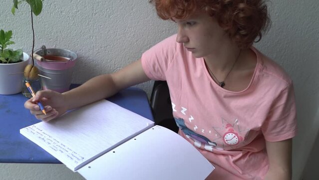 attractive female student makes notes in notebook while sitting on balcony