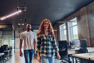 A woman with modern orange hair and an African American businessman walking together through the hallway of a contemporary coworking startup office, reflecting diversity and collaboration