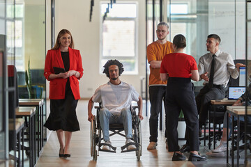 A group of young business people in a modern glass-walled office captures the essence of diversity and collaboration, while two colleagues, including an African American businessman in a wheelchair