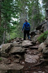 Person is trekking down a rugged trail surrounded by lush green trees in a forested area