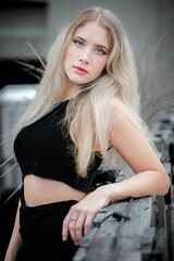 Fototapeta na wymiar Elegant blonde girl in a black dress with an exposed midriff posing in an urban environment