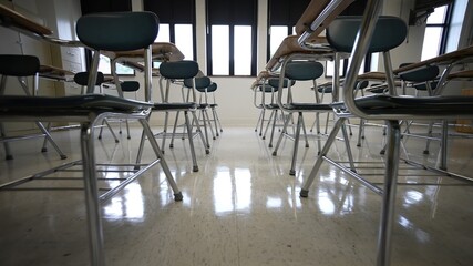 Rows of empty desks chairs in a school classroom towards the back of the room.