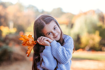 Autumn harvest of pumpkins. Child and orange pumpkin at farm market or seasonal festival. Cute little girl playing among pumpkins. Thanksgiving holiday season and Halloween.