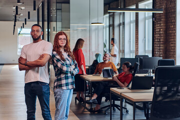 A young African American businessman and a modern businesswoman with orange hair stand side by side, arms crossed, exuding confidence and unity in a contemporary office setting, epitomizing dynamic