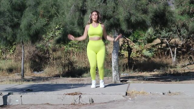 fitness woman in park doing jumping jacks in sportswear. sporty latin model