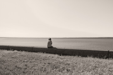 Lonely woman sits on the bank of a dam near the river