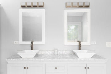 A bathroom detail with a white cabinet, two vessel sinks, marble countertop, and a bronze light fixture mounted above white framed mirrors.