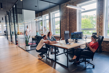 A diverse group of business professionals collaborates in a modern startup coworking center, utilizing a mix of paper-based and technological tools such as mobile phones and computers to collectively