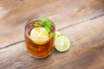 Glass of ice tea with green lemon slice with mint on wooden table. Top view of beverage.