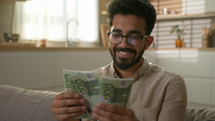 Happy Indian Arabian man rich businessman cash owner celebrate money win count dollars banknotes...