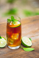 Glass of ice tea with lime slice with mint on wooden table