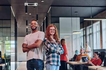 A young African American businessman and a modern businesswoman with orange hair stand side by side, arms crossed, exuding confidence and unity in a contemporary office setting, epitomizing dynamic