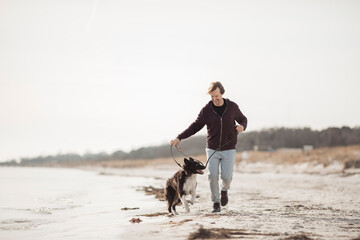 Middle aged caucasian man jogging and exercising on a beach with his border collie dog