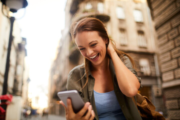 Young caucasian woman using a smart phone on a sidewalk in the city