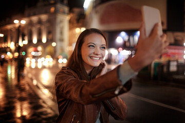Young caucasian woman taking a selfie at the piccadilly circus in London UK at night