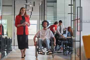 Obraz premium A group of young business people in a modern glass-walled office captures the essence of diversity and collaboration, while two colleagues, including an African American businessman in a wheelchair