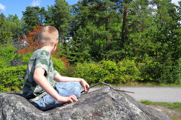 Child relaxing on a large rock one sunny summer day. Sweden, 2023.