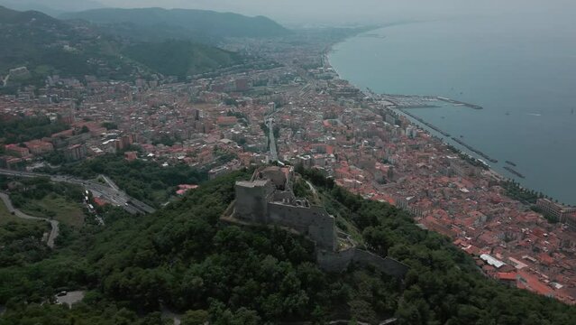 Drone shot over Arechi Castle on a green forested hill with sea view