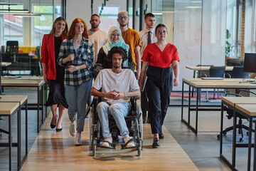 A diverse group of young business people walking a corridor in the glass-enclosed office of a modern startup, including a person in a wheelchair and a woman wearing a hijab, showing a dynamic mix of